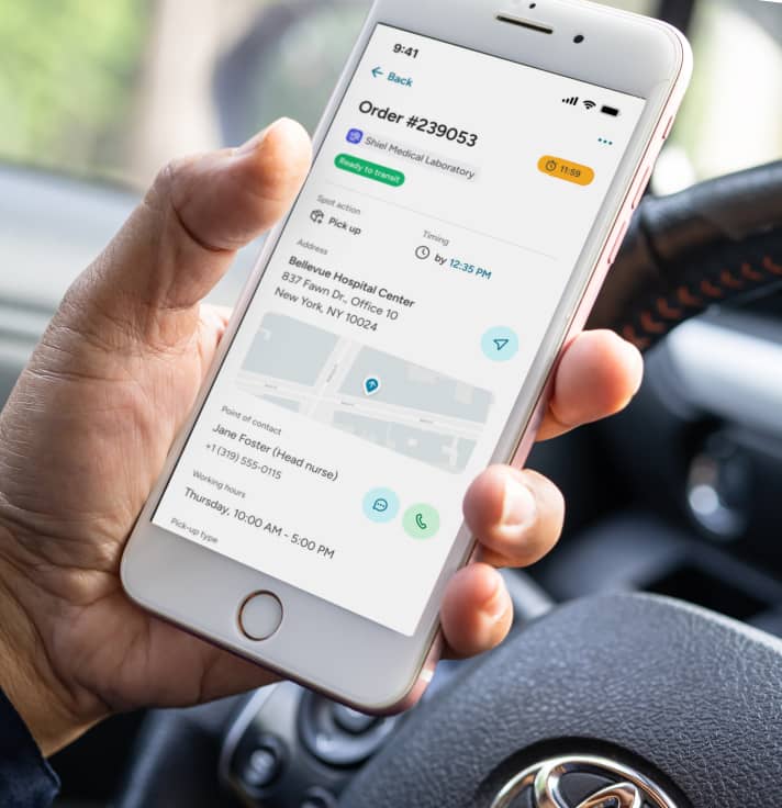 A driver holding a smartphone displaying an order details screen of the carGO Health app.