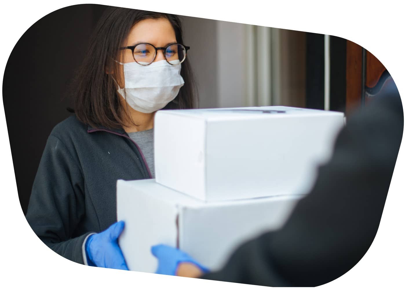 A woman wearing a mask receiving two white boxes from a medical courier.